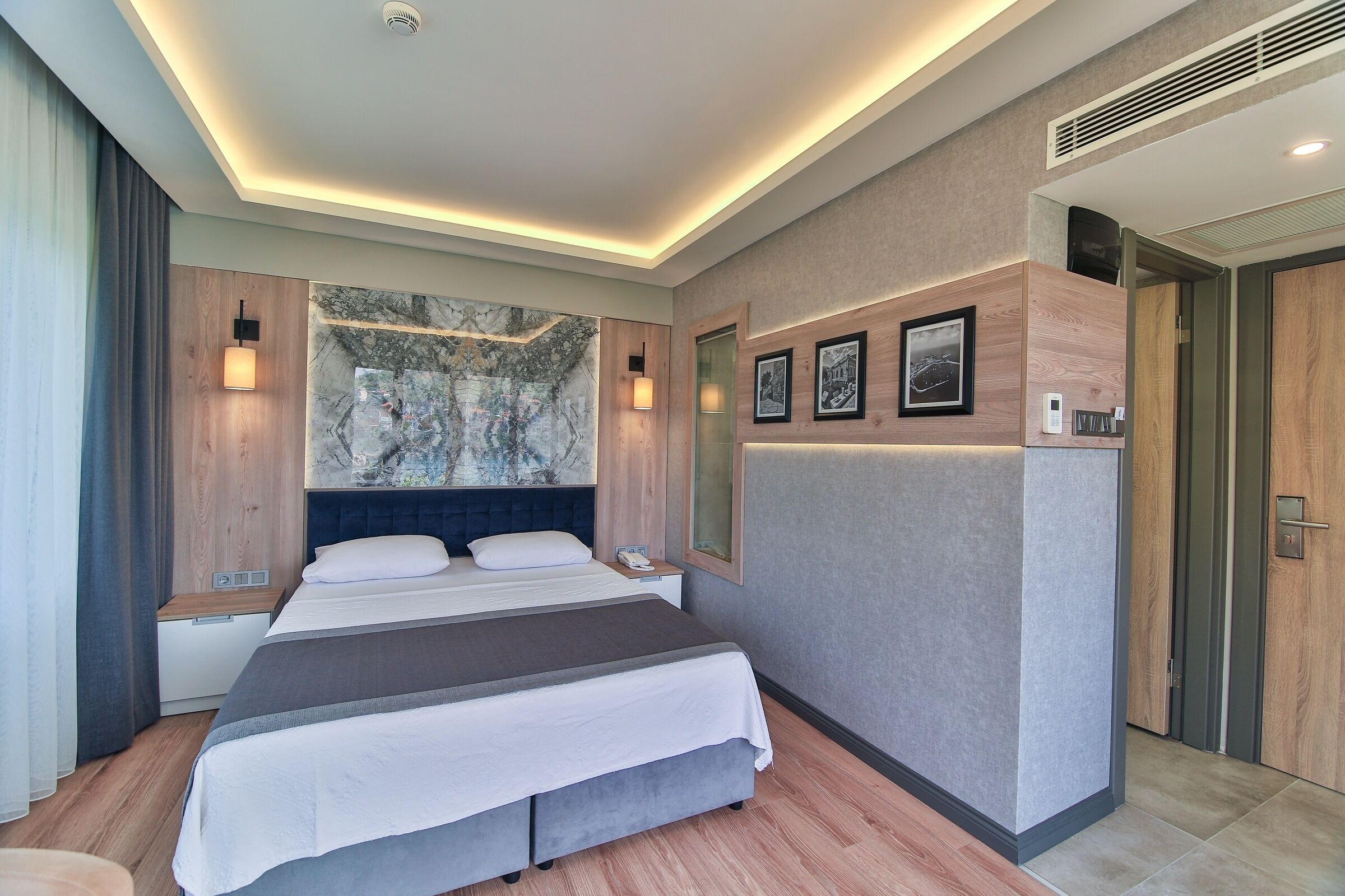 Une chambre d’hôtel moderne avec un grand lit, un mur décoratif en marbre et une tête de lit en bois.