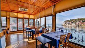 Un restaurante con amplios ventanales que ofrece vistas a un pueblo costero y al mar.