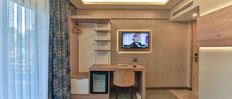 A hotel room with a bed, a desk with a TV, a mini-fridge, and a wardrobe.