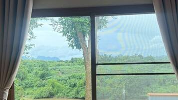 A bedroom with a large window, a bed, and a view of a lush landscape.