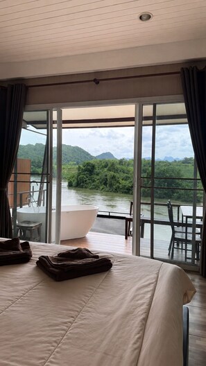 Une chambre d’hôtel avec un grand lit, une baignoire et une vue sur une rivière et des montagnes.