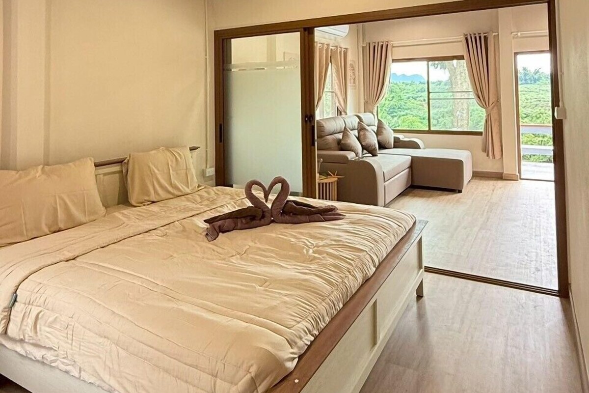 A bedroom with a large bed, wooden ceiling beams, a view of the outdoors through a sliding door, and a ceiling fan.