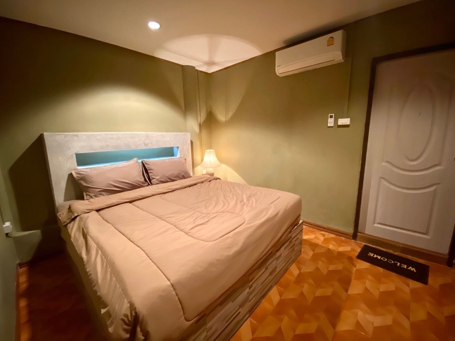 Ein Schlafzimmer mit einem Bett, einem Nachttisch, einer Lampe, einer Klimaanlage und einer Tür.