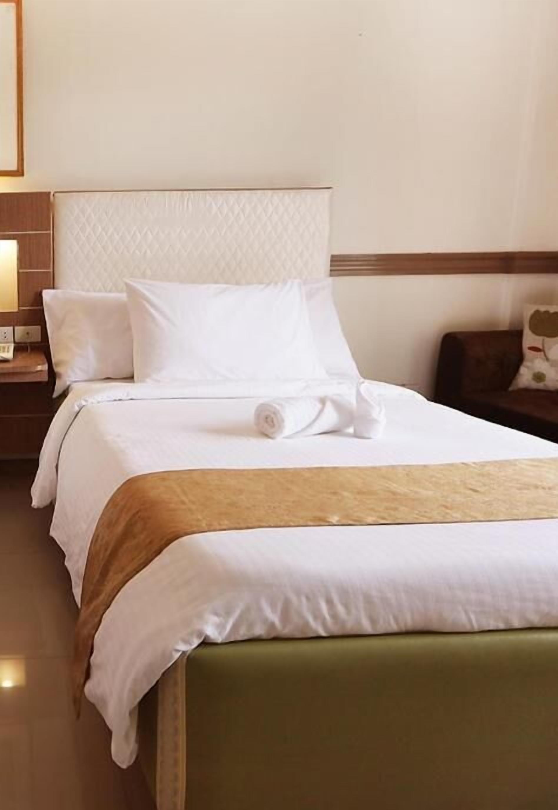 Habitación de hotel con una cama grande, una mesita de noche de madera y un cabecero tapizado de color verde.