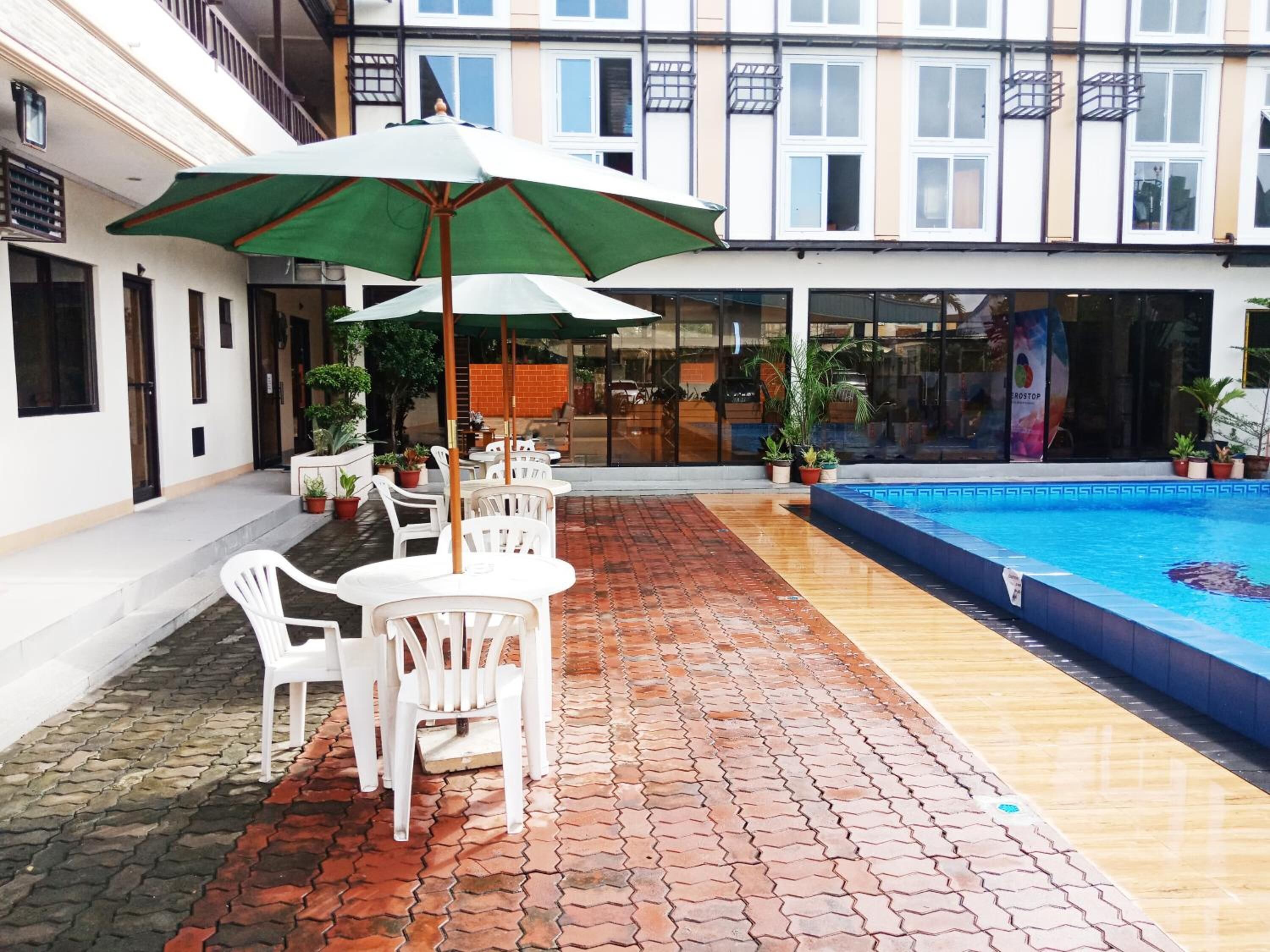 An outdoor patio area with a swimming pool, white plastic chairs, and a green umbrella.