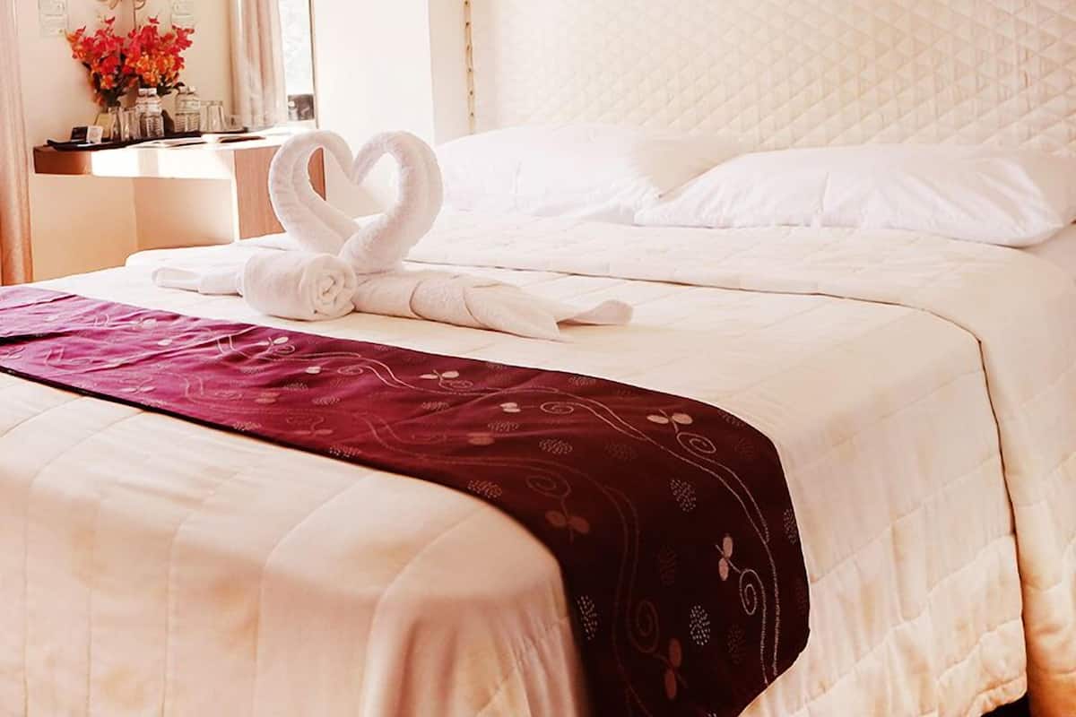 A hotel room with a neatly made bed, a heart-shaped towel arrangement, a mirror, and a bedside table with toiletries.