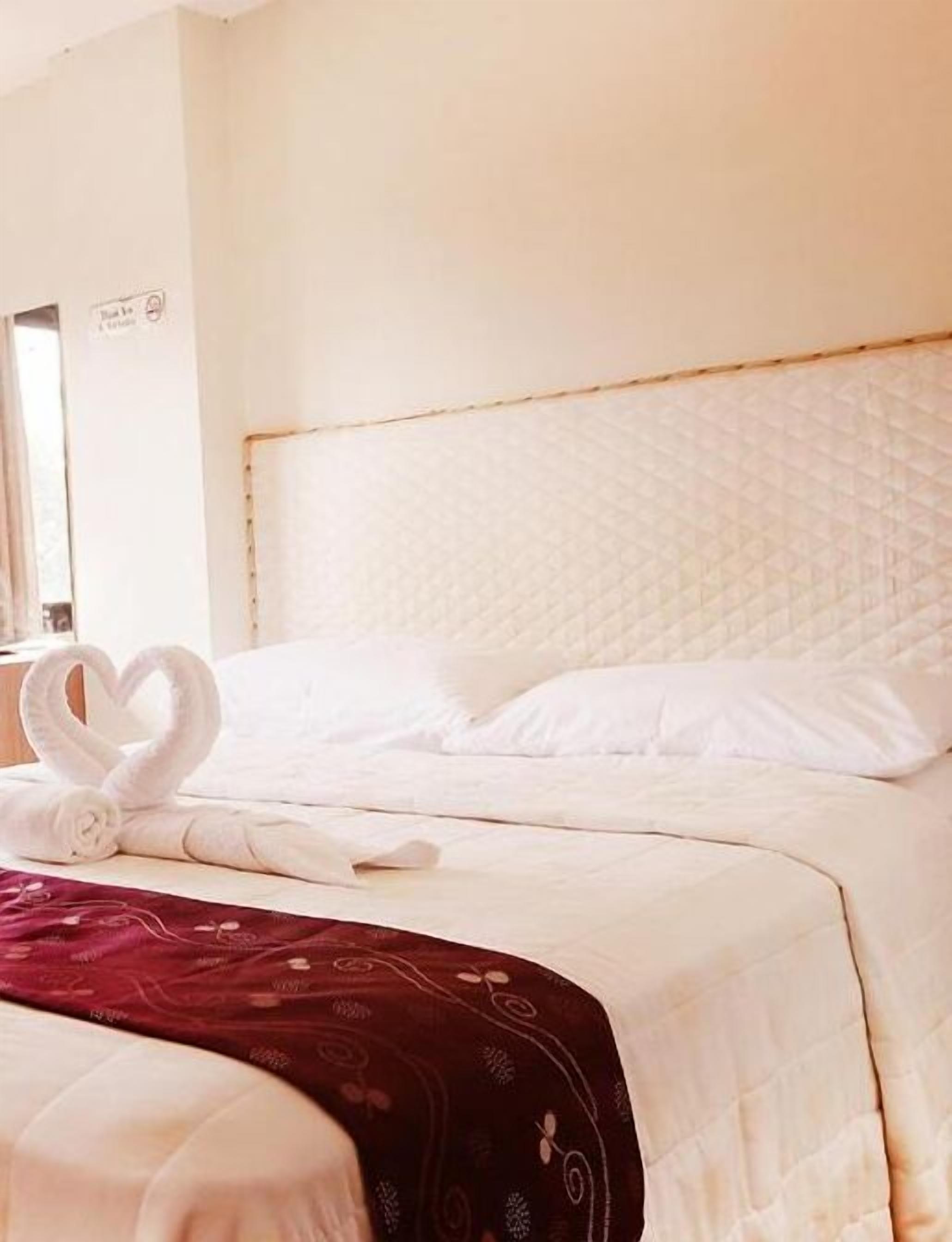 Hotellihuone, jossa on suuri sänky, valkoiset vuodevaatteet ja sydämenmuotoinen pyyheasetelma sängyllä.