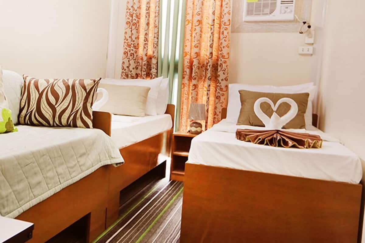A hotel room with two single beds, a small table, and a window with curtains.