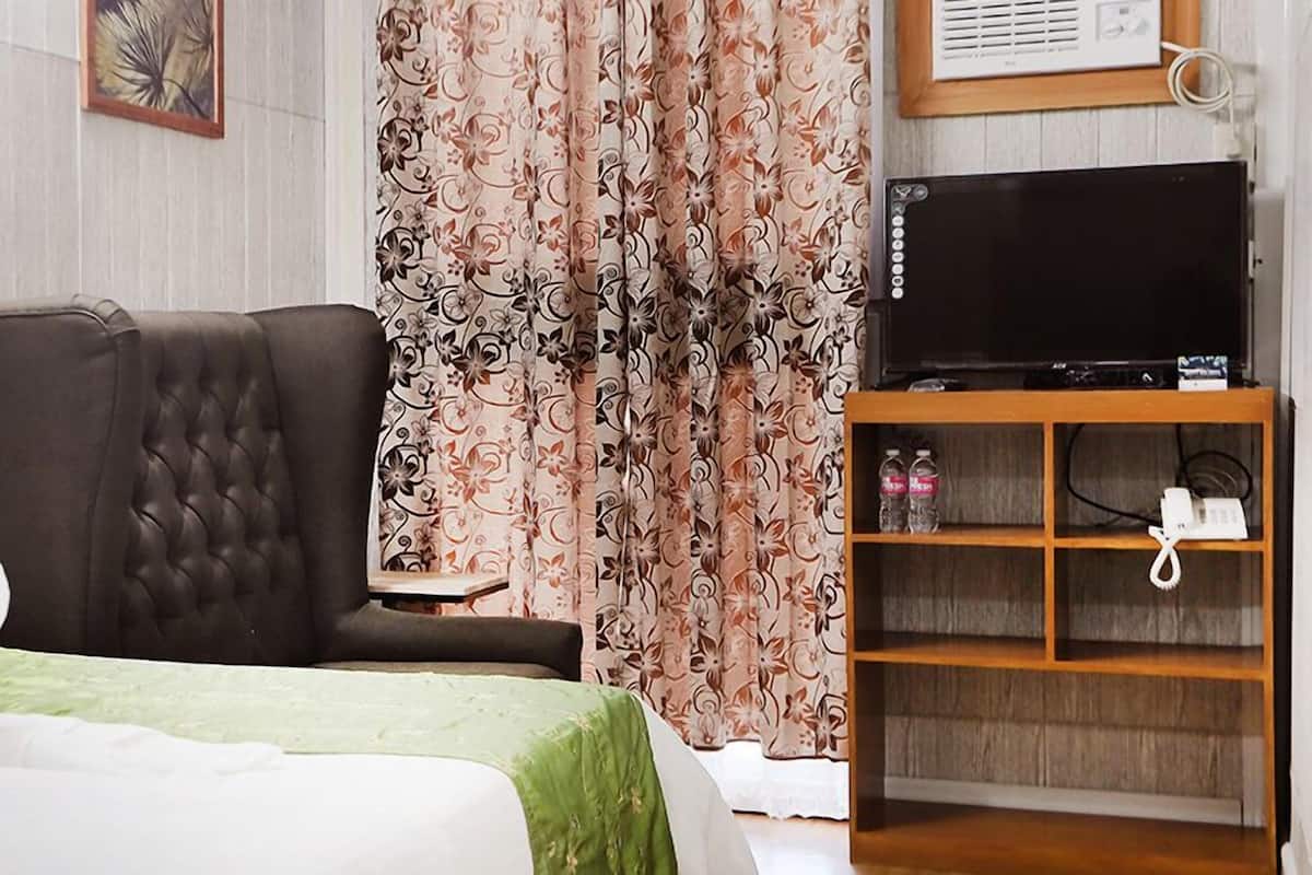 A bedroom with a bed, a sofa, a TV on a wooden stand, and a curtain with a floral pattern.