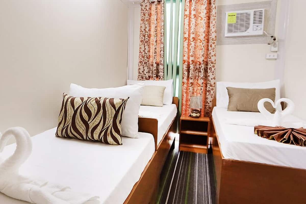 A hotel room with two single beds, a small table with a lamp, and a window with curtains.