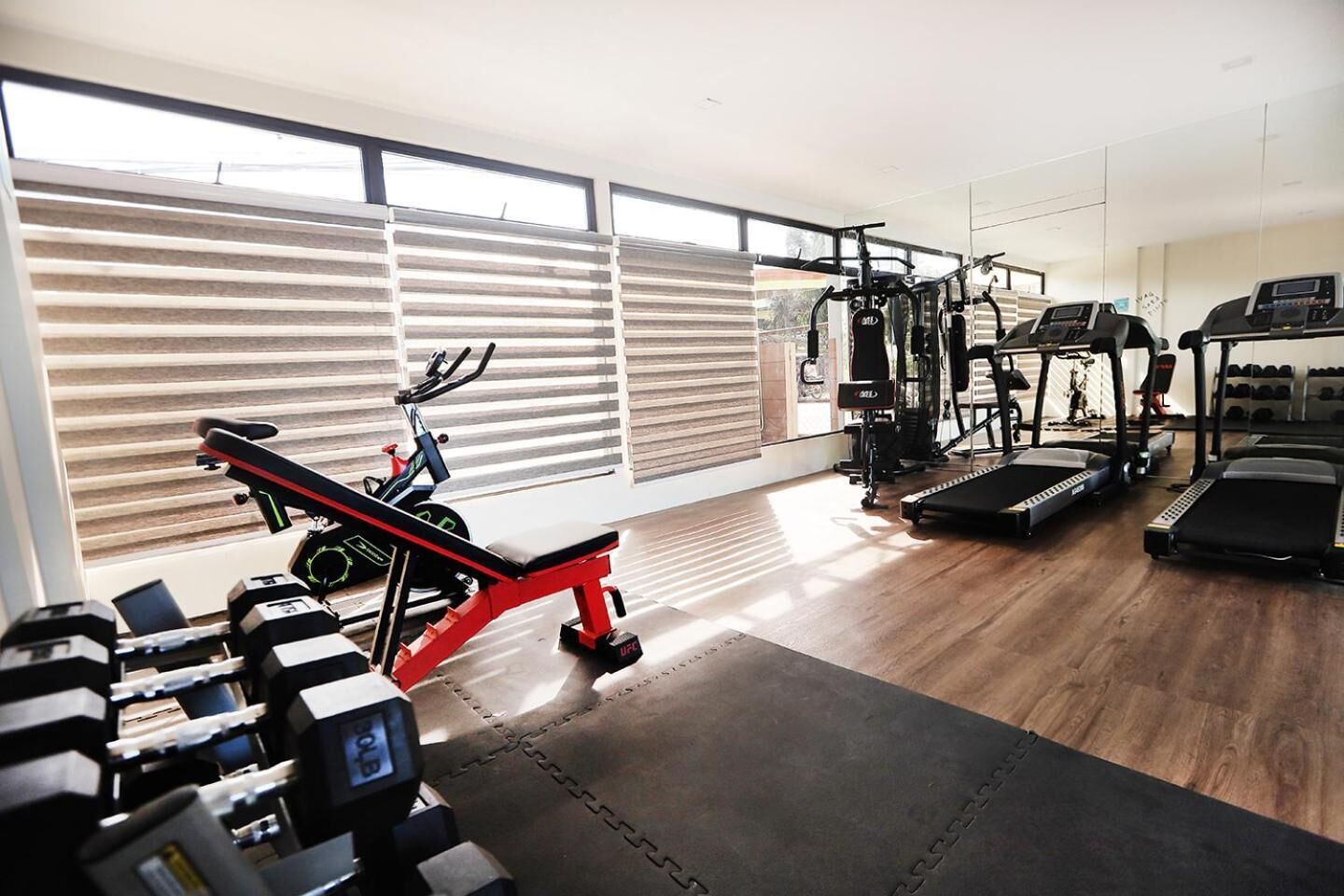 Un gimnasio moderno con máquinas de cardio, equipo de levantamiento de pesas y un amplio ventanal con persianas.