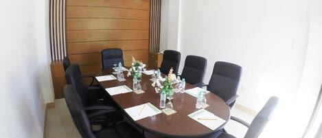 A conference room with a wooden panel wall, a round table, and six black office chairs.