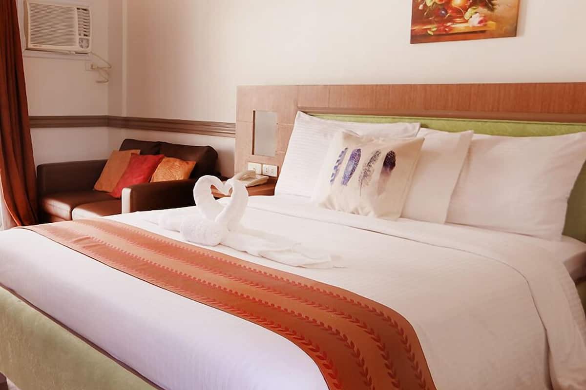 A neatly made bed with a swan-shaped towel, a green and orange bedspread, and a painting on the wall.