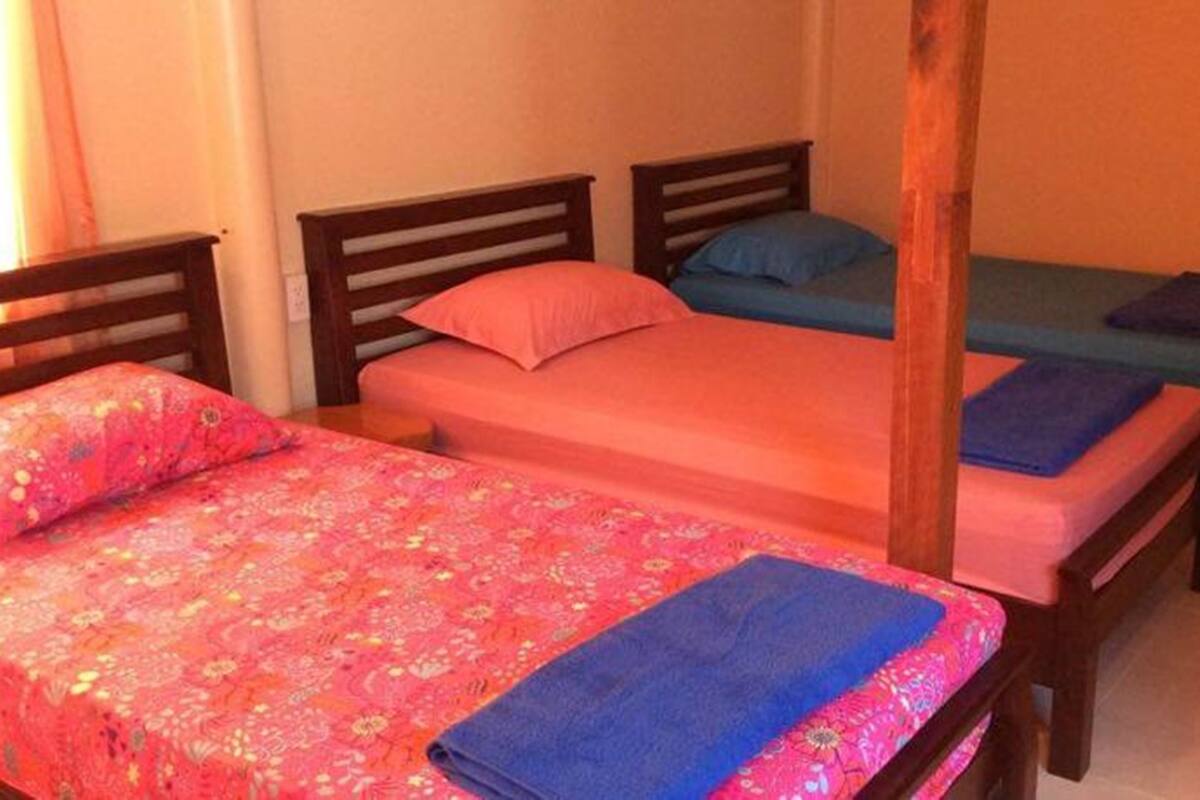 Een kamer met drie bedden, elk met een andere kleur sprei en kussens.