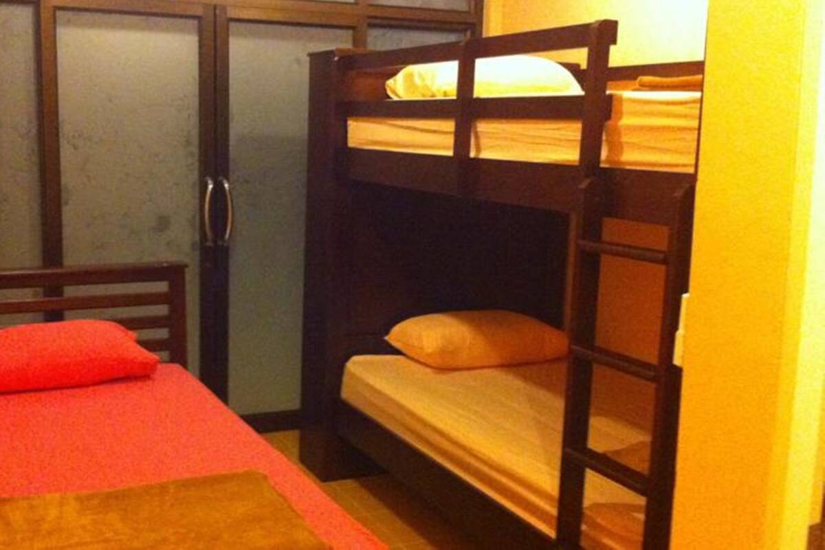Een kleine, compacte kamer met een stapelbed, een enkel bed en een deur.