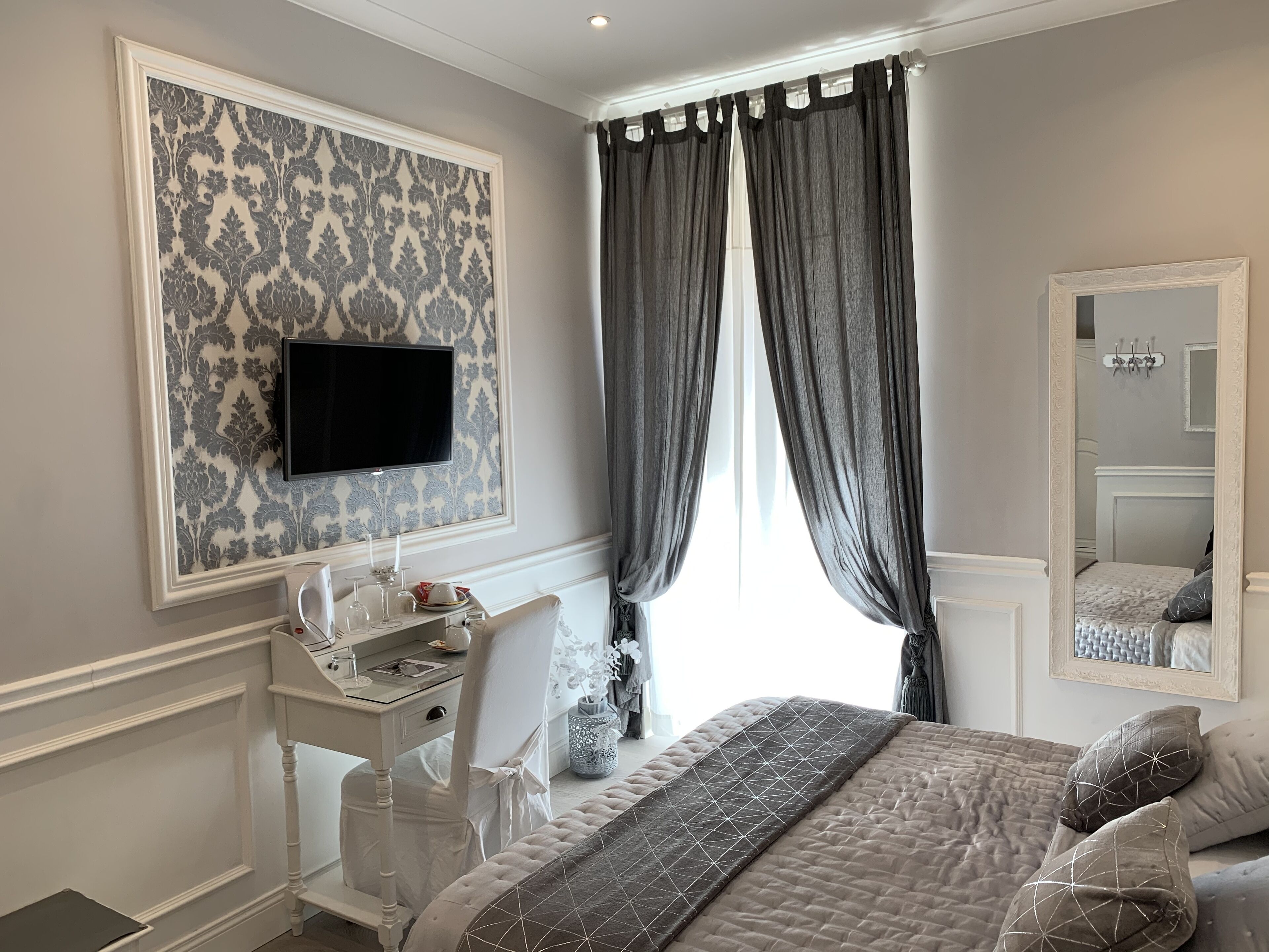 A bedroom with a bed, a desk, a chair, a TV, and a window with curtains.