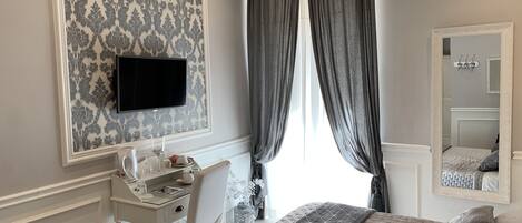 A bedroom with a bed, a desk, a chair, a TV, and a window with curtains.