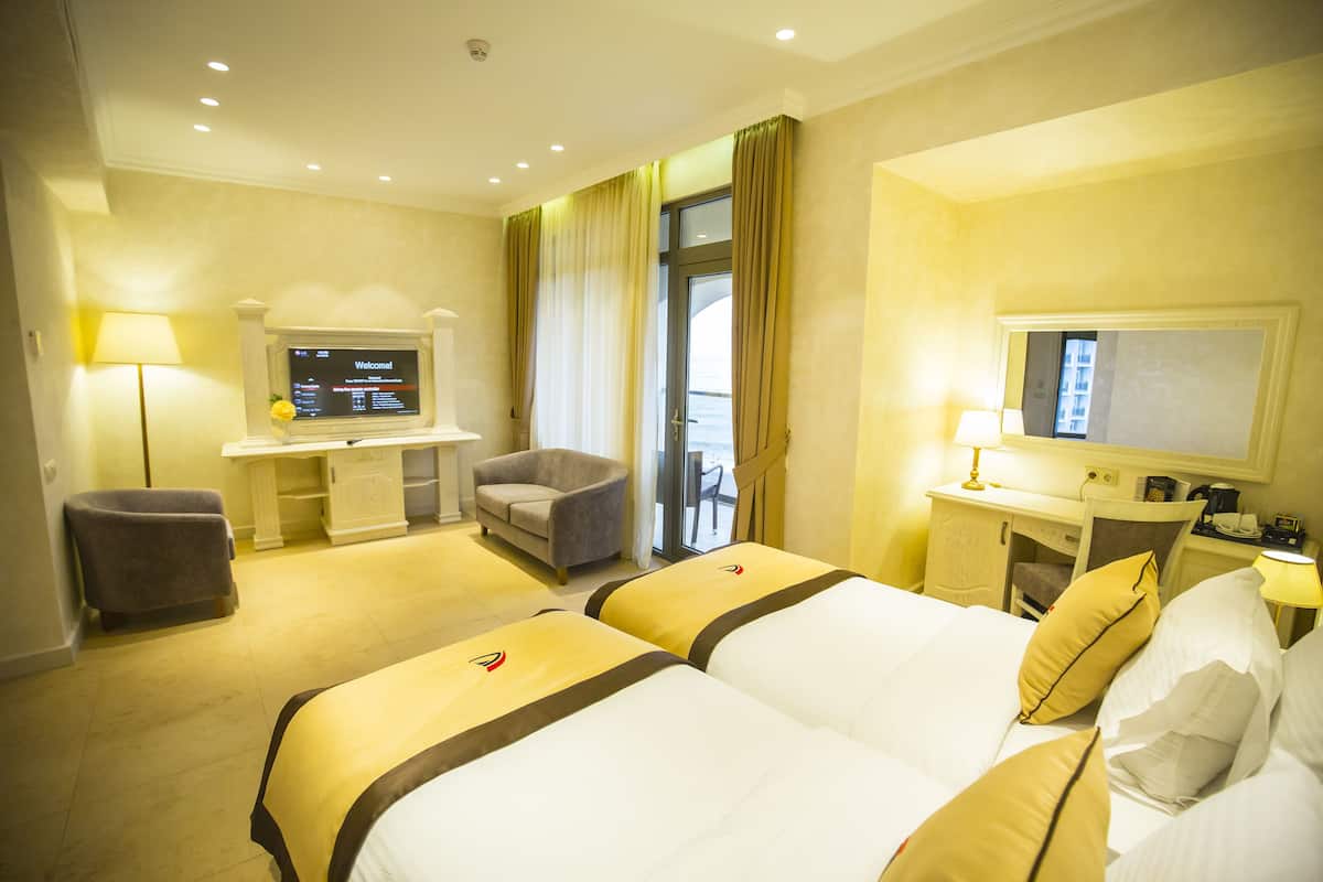 A hotel room with two beds, a desk, a chair, a television, and a view of the outdoors.