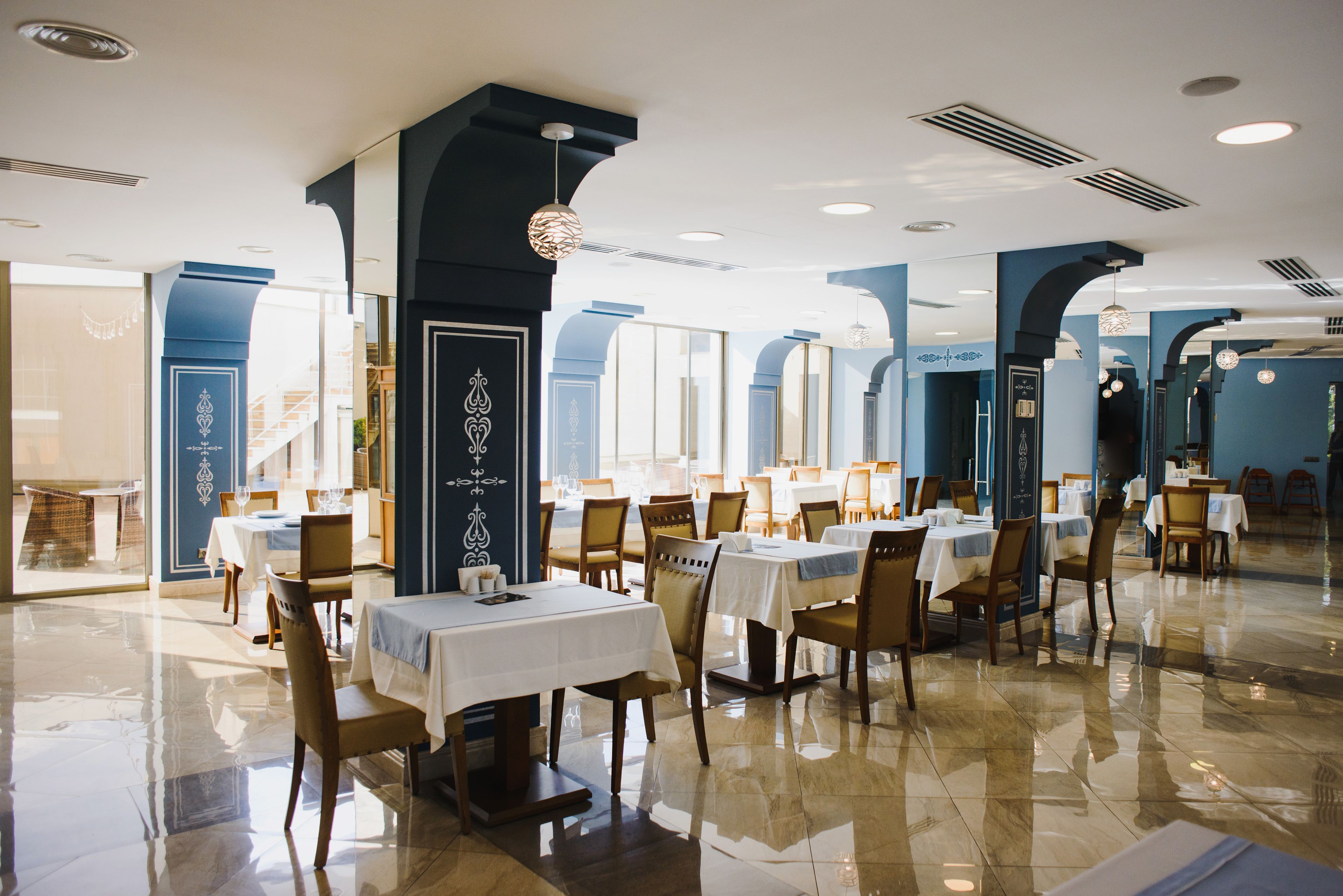 Un restaurante espacioso con numerosas mesas y sillas, ventanas amplias y suelo pulido.