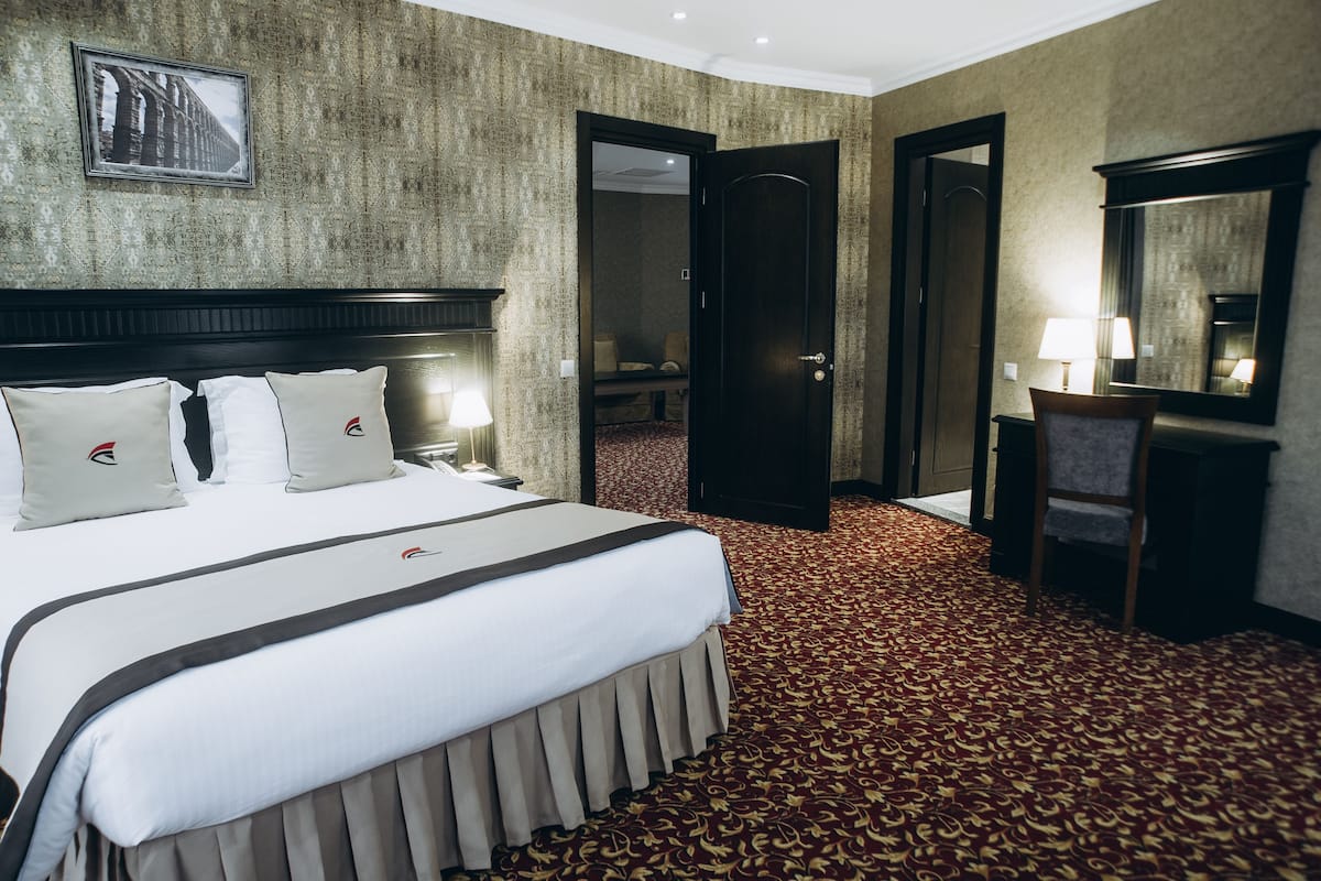 A hotel room with a large bed, a desk, a chair, a mirror, and a carpeted floor.