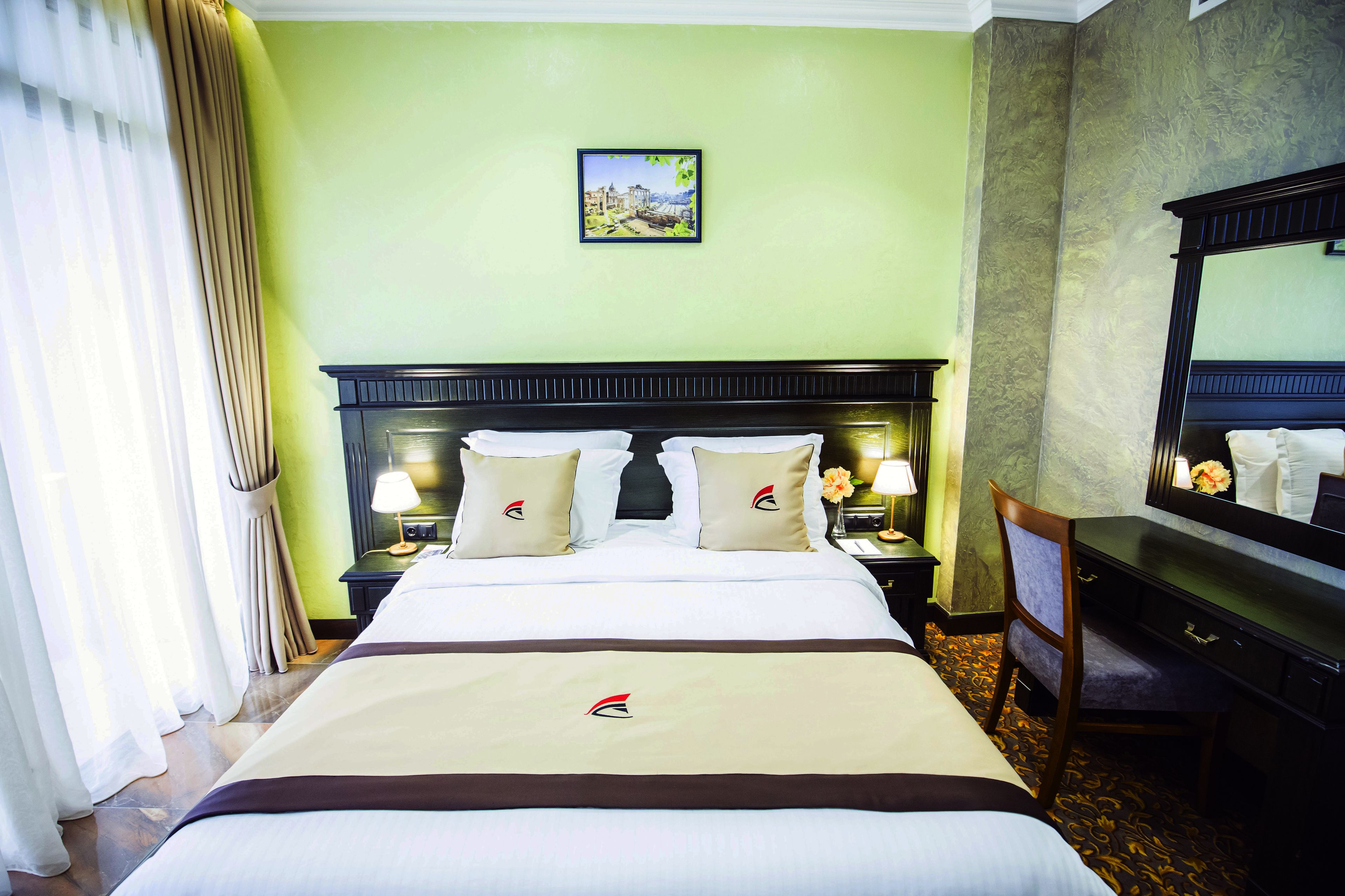 A hotel room with a large bed, a nightstand with a lamp, a dresser, and a mirror.