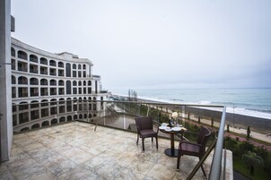 Un balcón con vistas al océano, una mesa de comedor con sillas y un edificio con varios balcones al fondo.