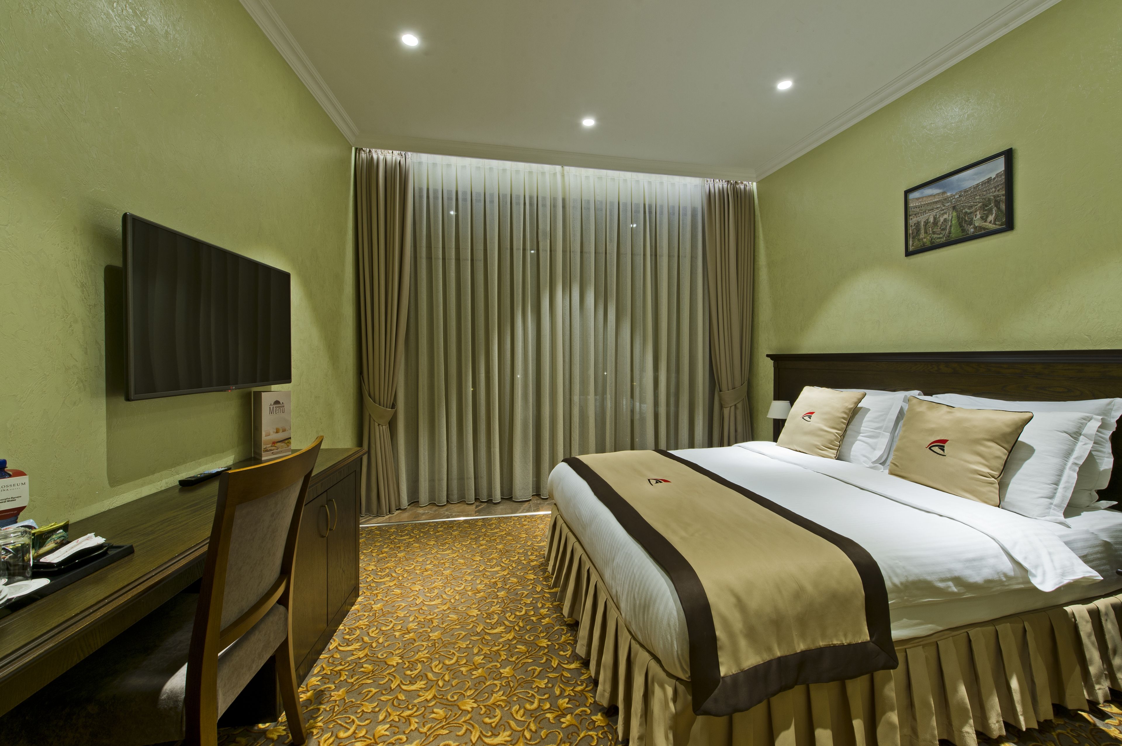 A hotel room with a bed, a desk, a television, and a large window with curtains.