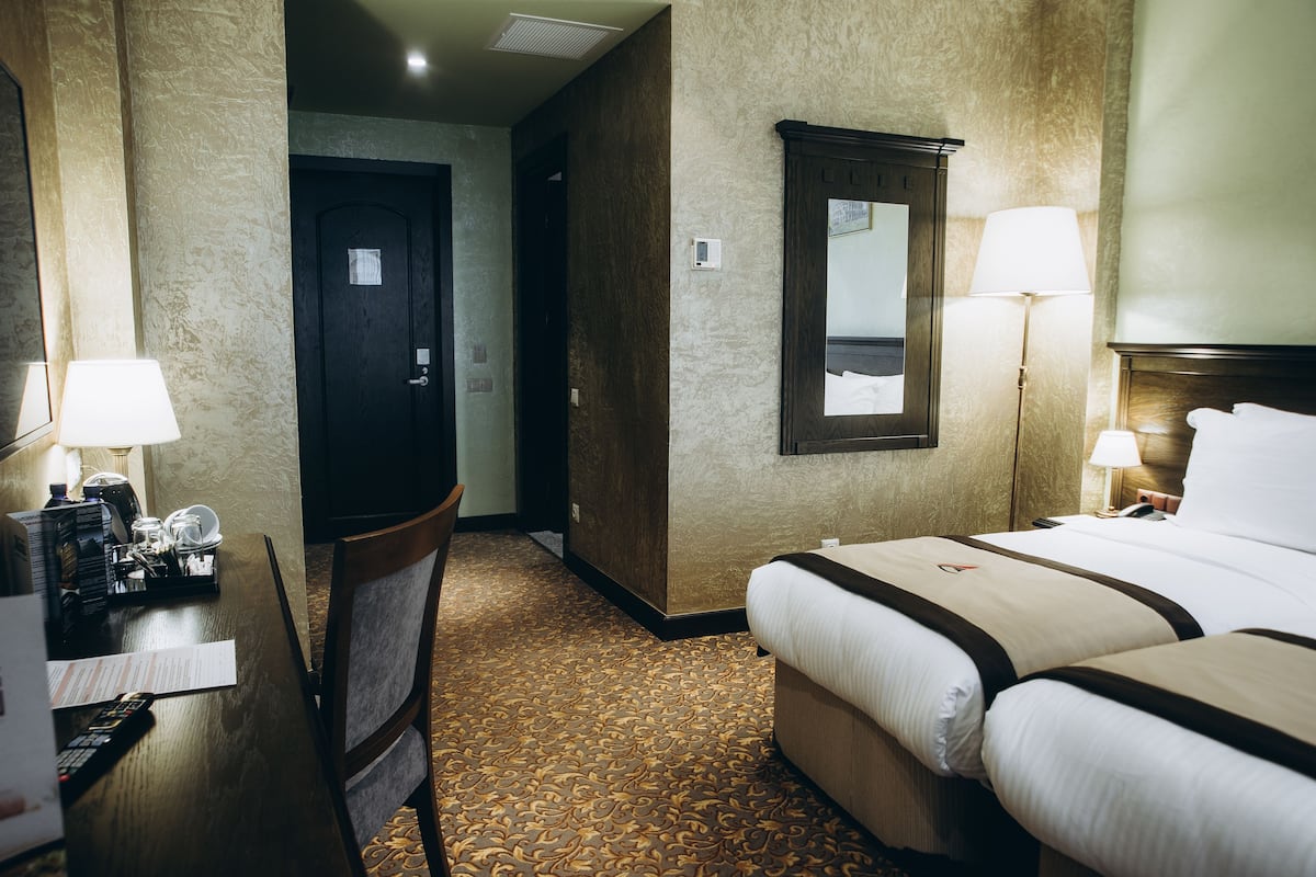 A hotel room with a bed, bedside table, lamp, and a mirror.