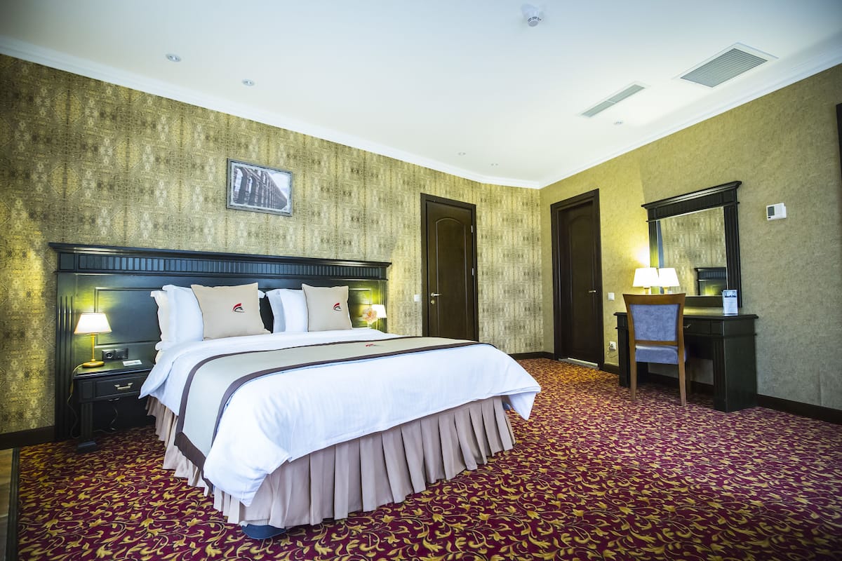 A hotel room with a large bed, a desk, a chair, and a mirror.