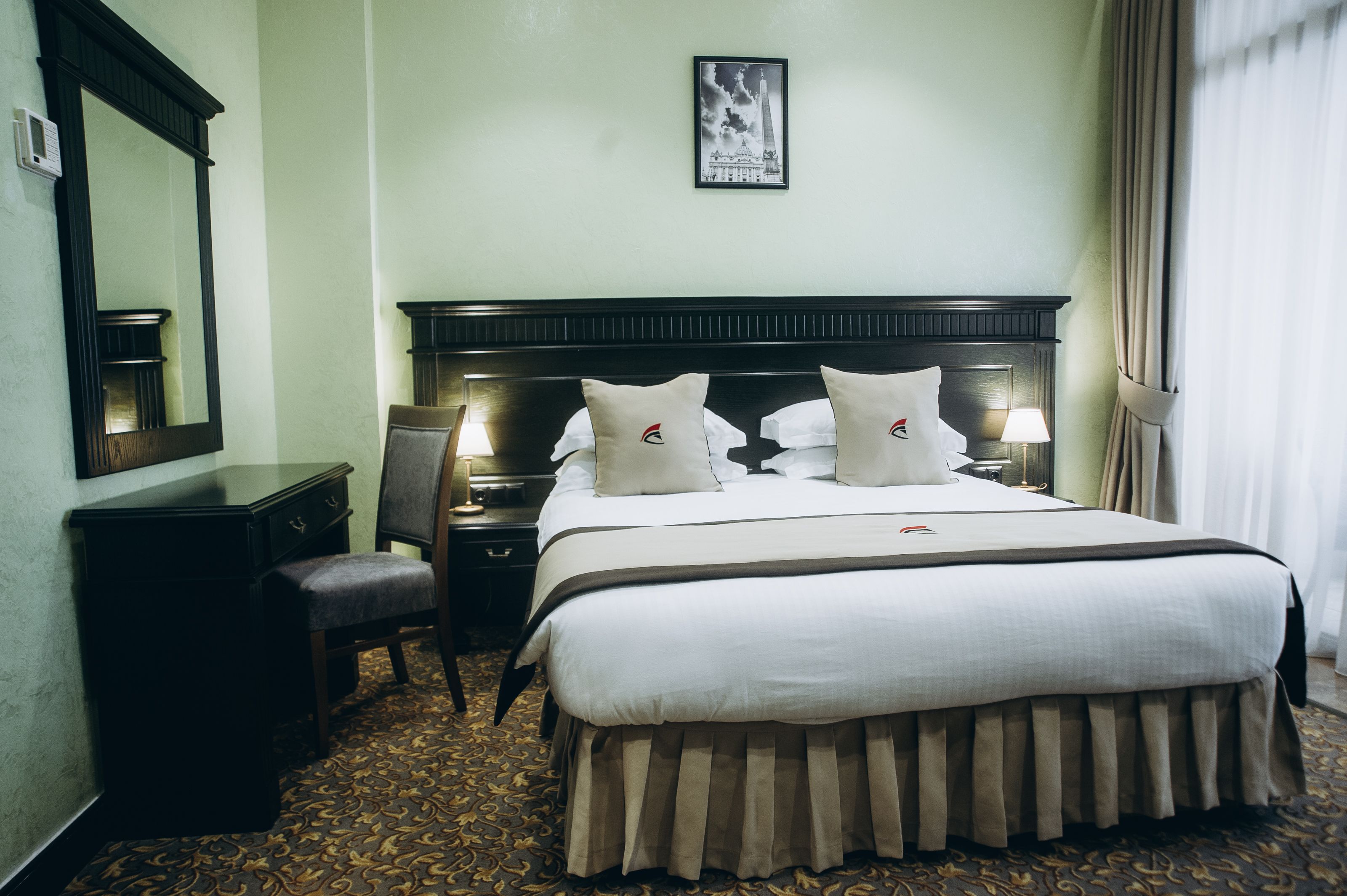 A hotel room with a large bed, two bedside tables with lamps, a chair, a desk, and a large mirror.