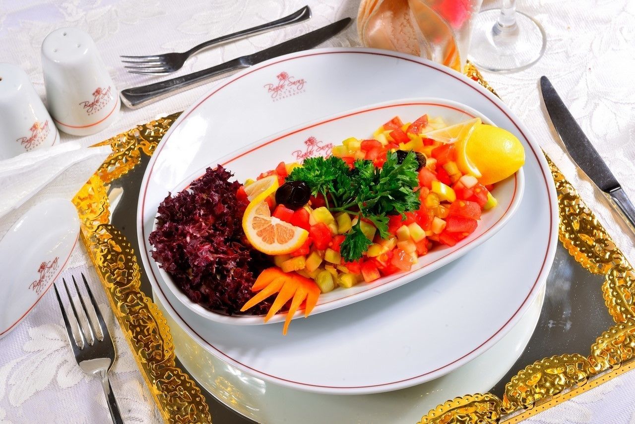 A plated meal with a variety of vegetables and a lemon wedge, served on a white plate with a gold rim.