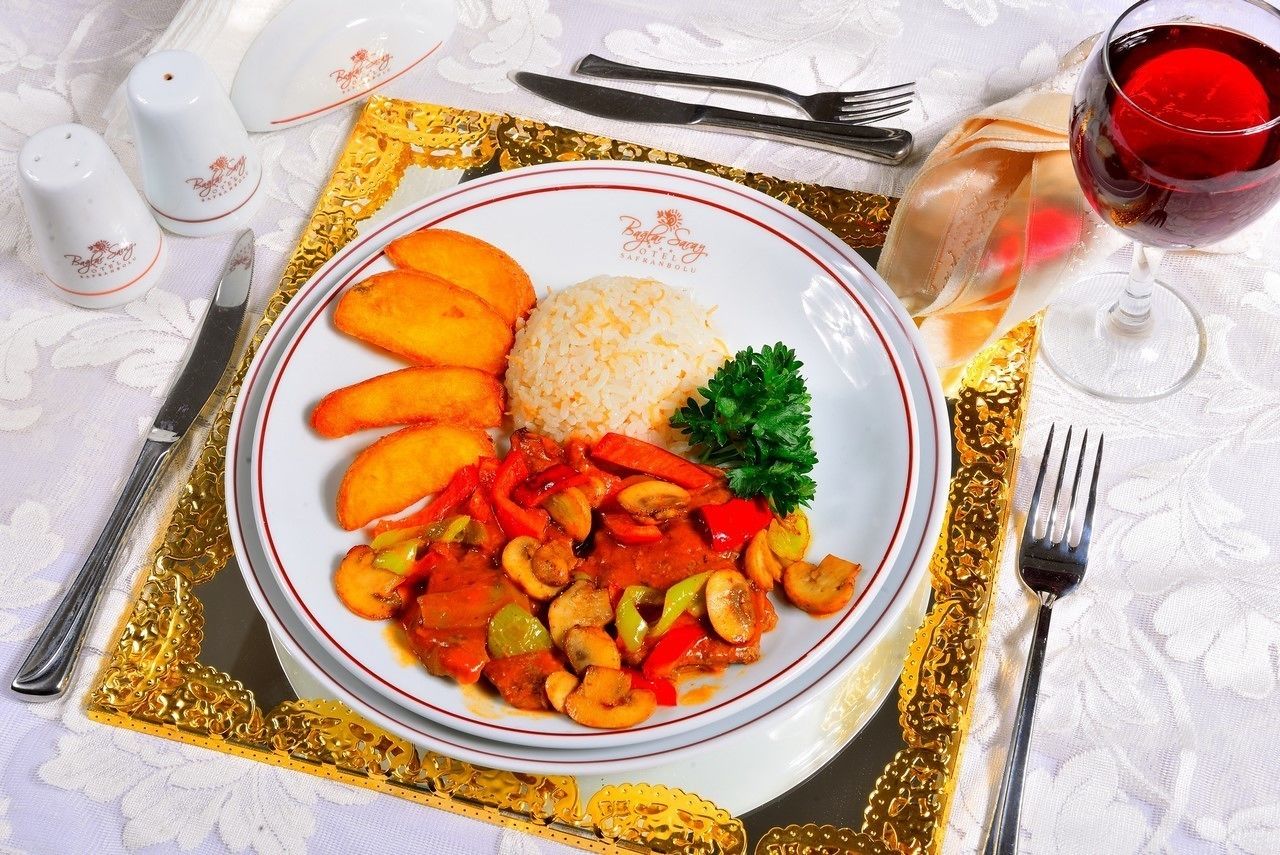 A plate of food with rice, sliced vegetables, and mushrooms, accompanied by a glass of red wine, on a table with a gold-trimmed tablecloth.