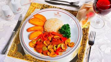 A plate of food with rice, sliced vegetables, and mushrooms, accompanied by a glass of red wine, on a table with a gold-trimmed tablecloth.