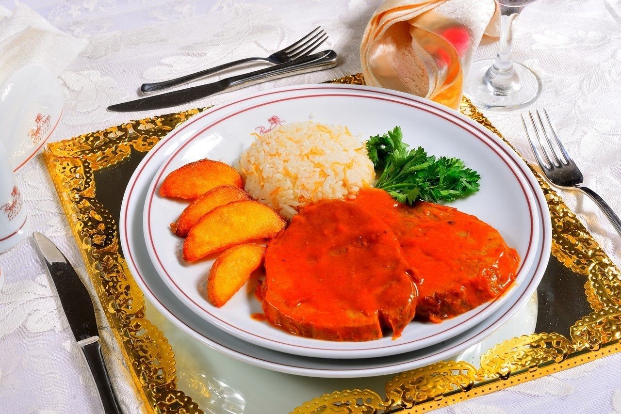 A plate of food with a slice of meat, rice, and roasted potatoes.