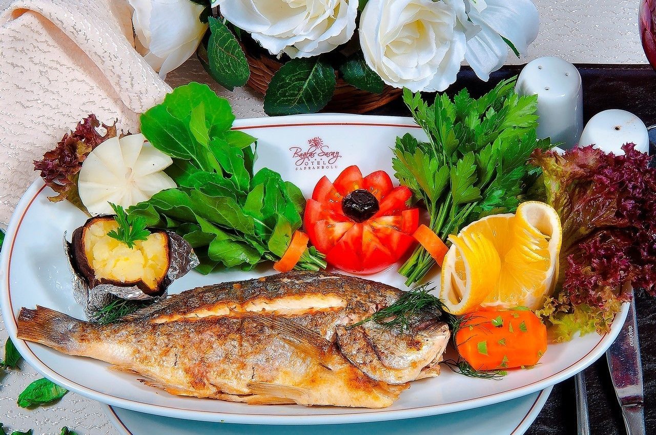 A plate with grilled fish, vegetables, and a decorative flower arrangement.