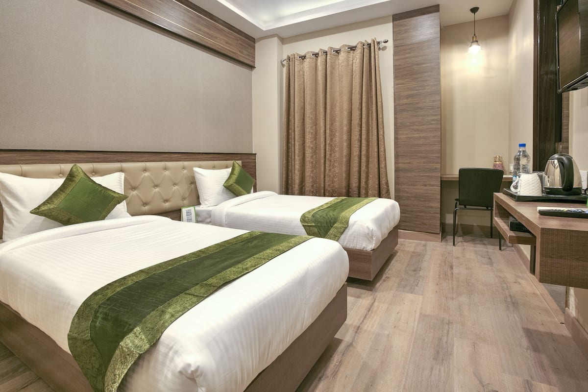 A hotel room with two beds, a desk, a chair, a television, and a curtain.