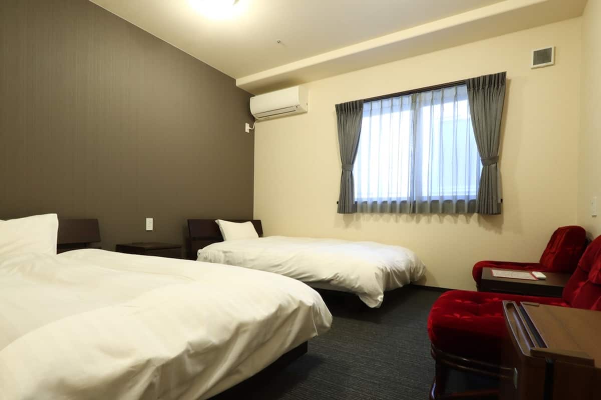 Hotellihuone, jossa on kaksi sänkyä, työpöytä, tuoli ja ikkuna, jossa on verhot.