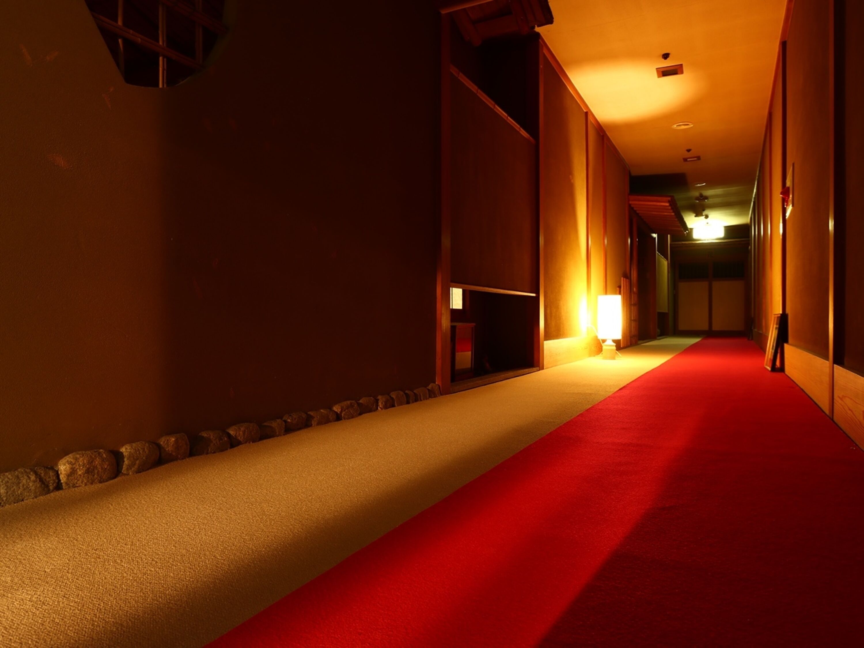 Un pasillo con alfombra roja, paredes de madera y una lámpara encendida.