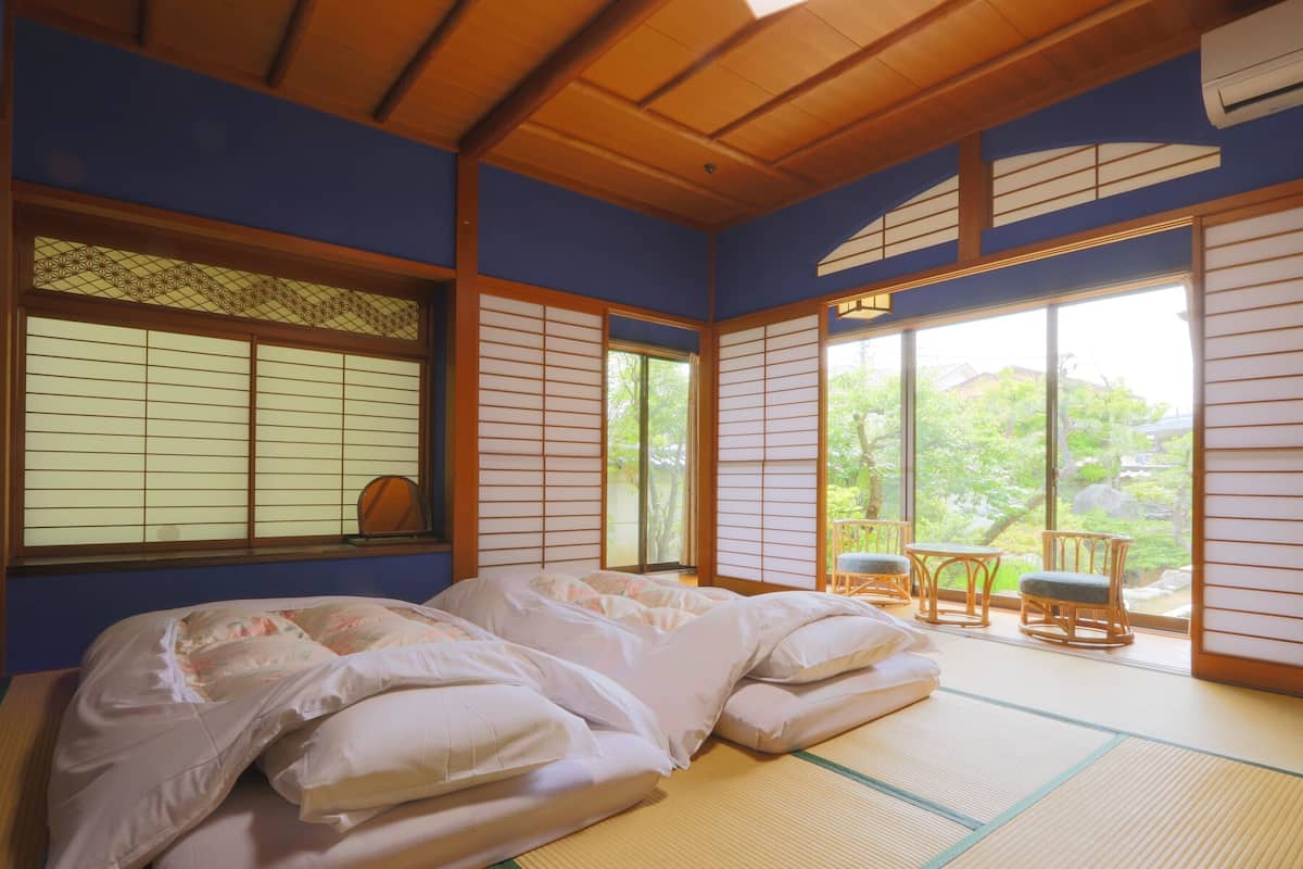 Perinteinen japanilaistyylinen huone, jossa on tatamimatto, valkoisilla tekstiileillä varustettu sänky ja liukuvat shoji-ovet.