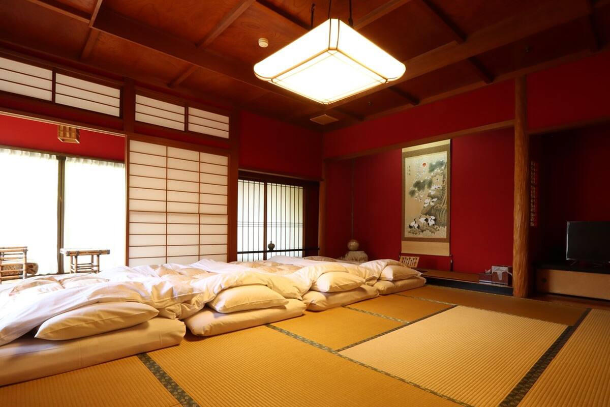 Perinteinen japanilaistyylinen huone, jossa on tatamimatot, matala sänky tyynyineen, liukuseinät ja taulu seinällä.