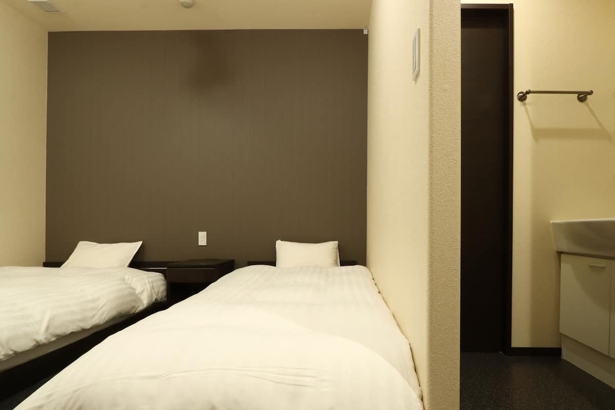 Hotellihuone, jossa on kaksi erillistä sänkyä, pieni yöpöytä, seinään kiinnitetty valaisin sekä kylpyhuone, jossa on pesuallas ja peili.