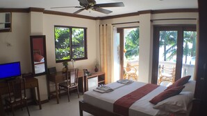 Habitación de hotel con cama, escritorio, silla, televisor y balcón con sillas.