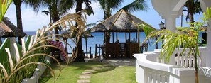 A beachside patio with a thatched-roof gazebo, palm trees, and a view of the ocean. - The Beach House (Carabao Island)