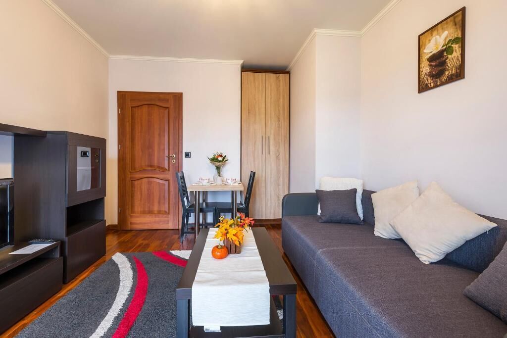 A modern living room with a sofa, a TV, a dining table with chairs, and a wooden wardrobe.