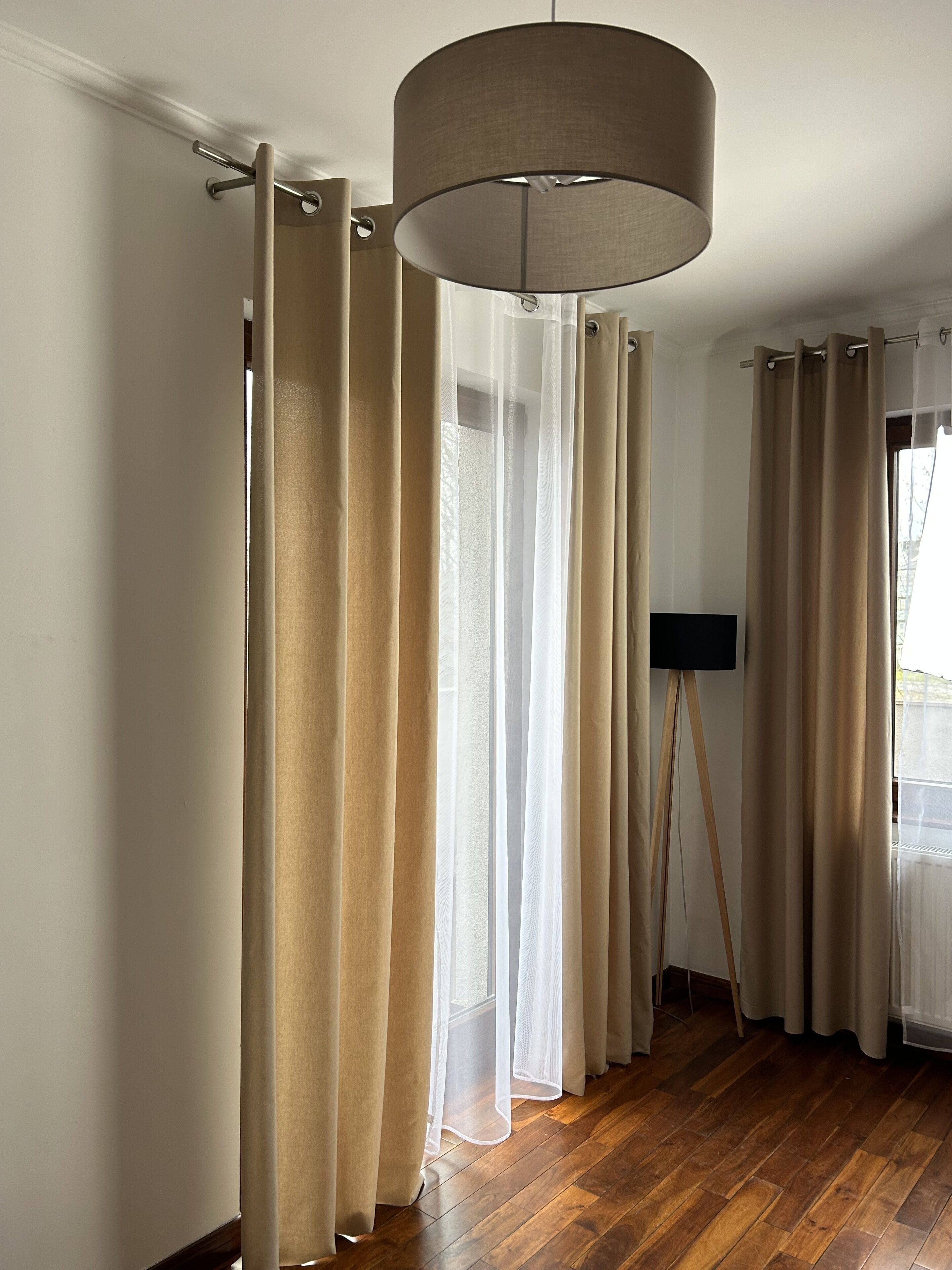A room with wooden flooring, beige curtains, and a ceiling lamp.