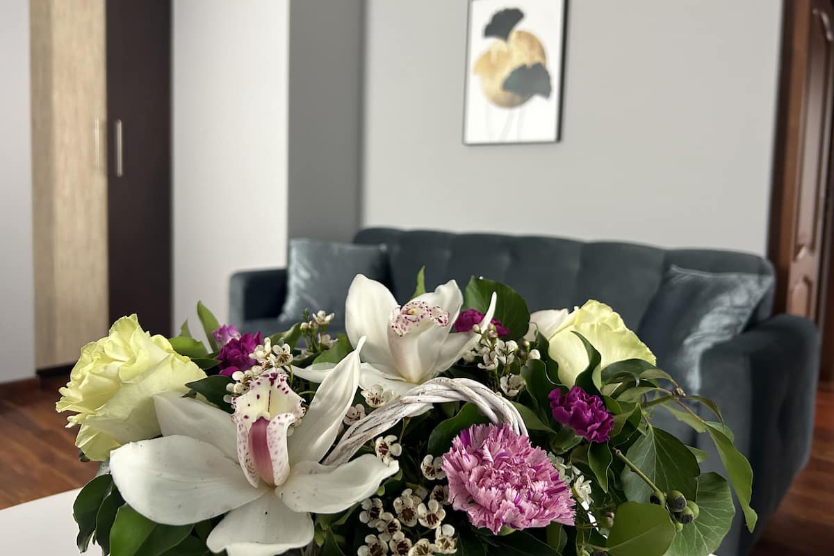Une pièce avec un canapé gris, un vase blanc rempli de fleurs et un tableau encadré accroché au mur.
