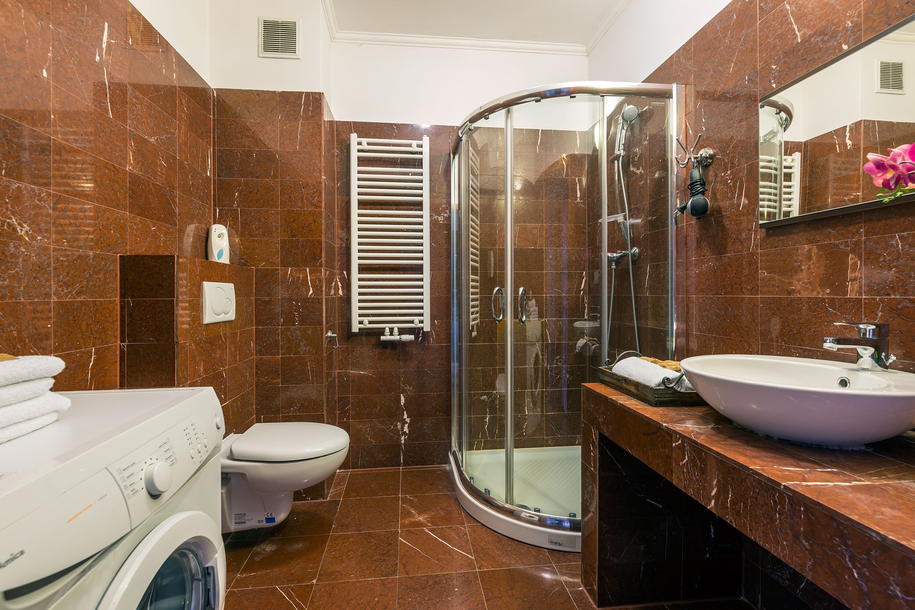A bathroom with a glass-enclosed shower, a white sink, and a washing machine.
