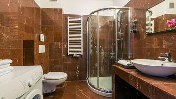 A bathroom with a glass-enclosed shower, a white sink, and a washing machine.