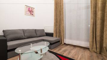 A modern living room with a grey sofa, a glass coffee table, and a red and black rug.