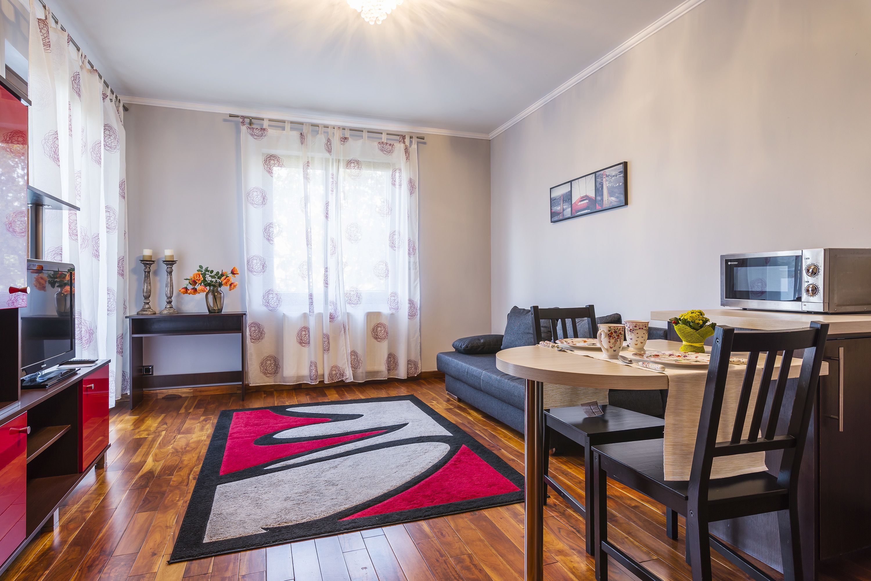 Uma sala de estar moderna com área de jantar, piso de madeira, TV e micro-ondas.